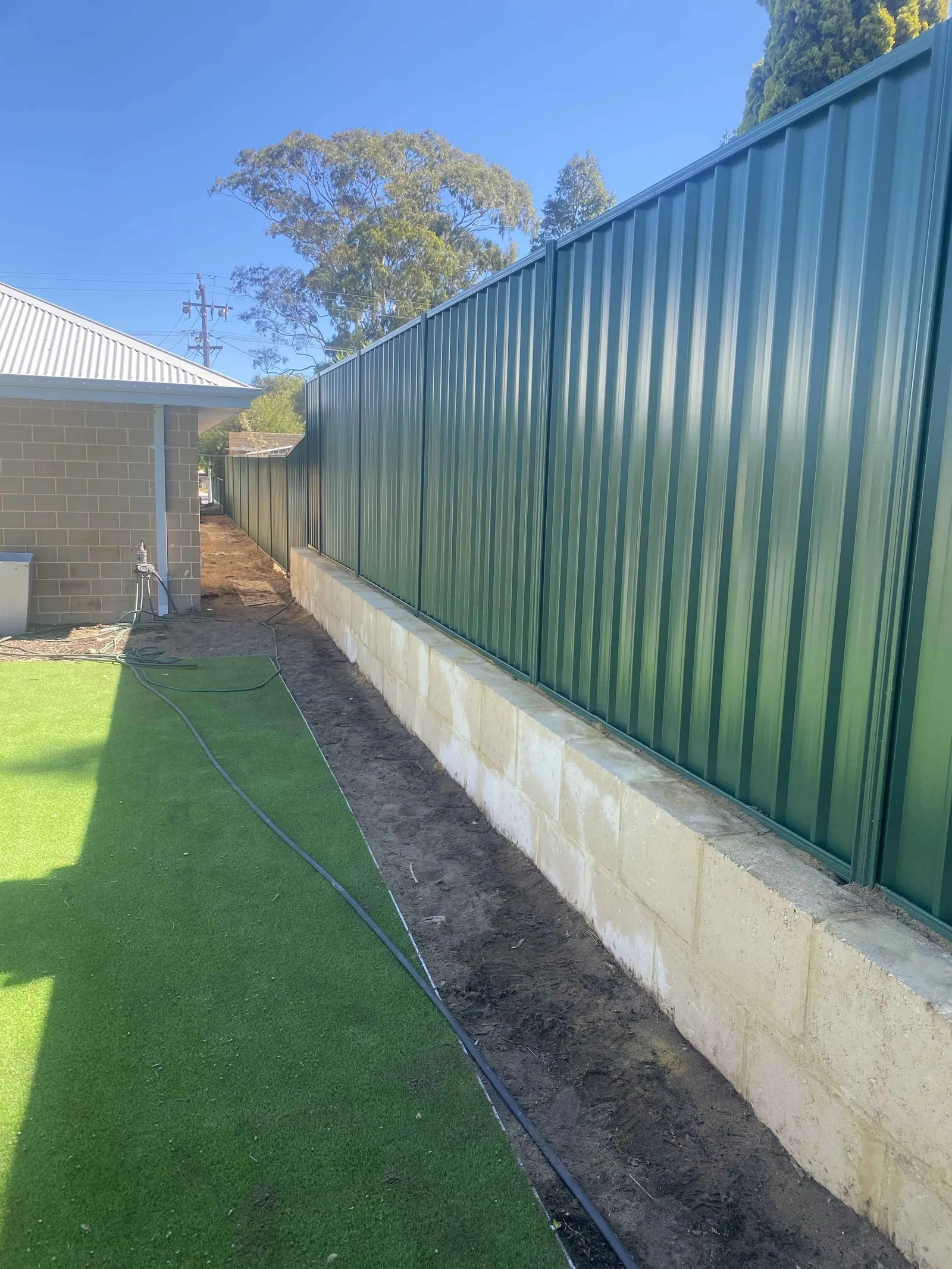 Limestone block retaining wall under a green Colorbond fence on a Perth side boundary