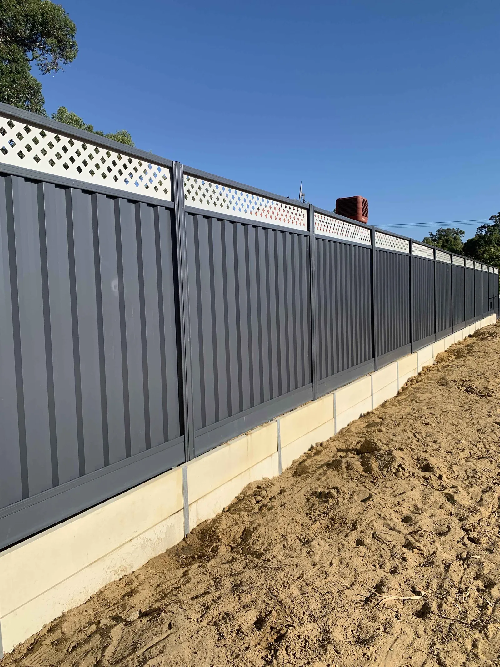 Panel retaining wall with a lattice-topped Colorbond fence and fresh sand backfill
