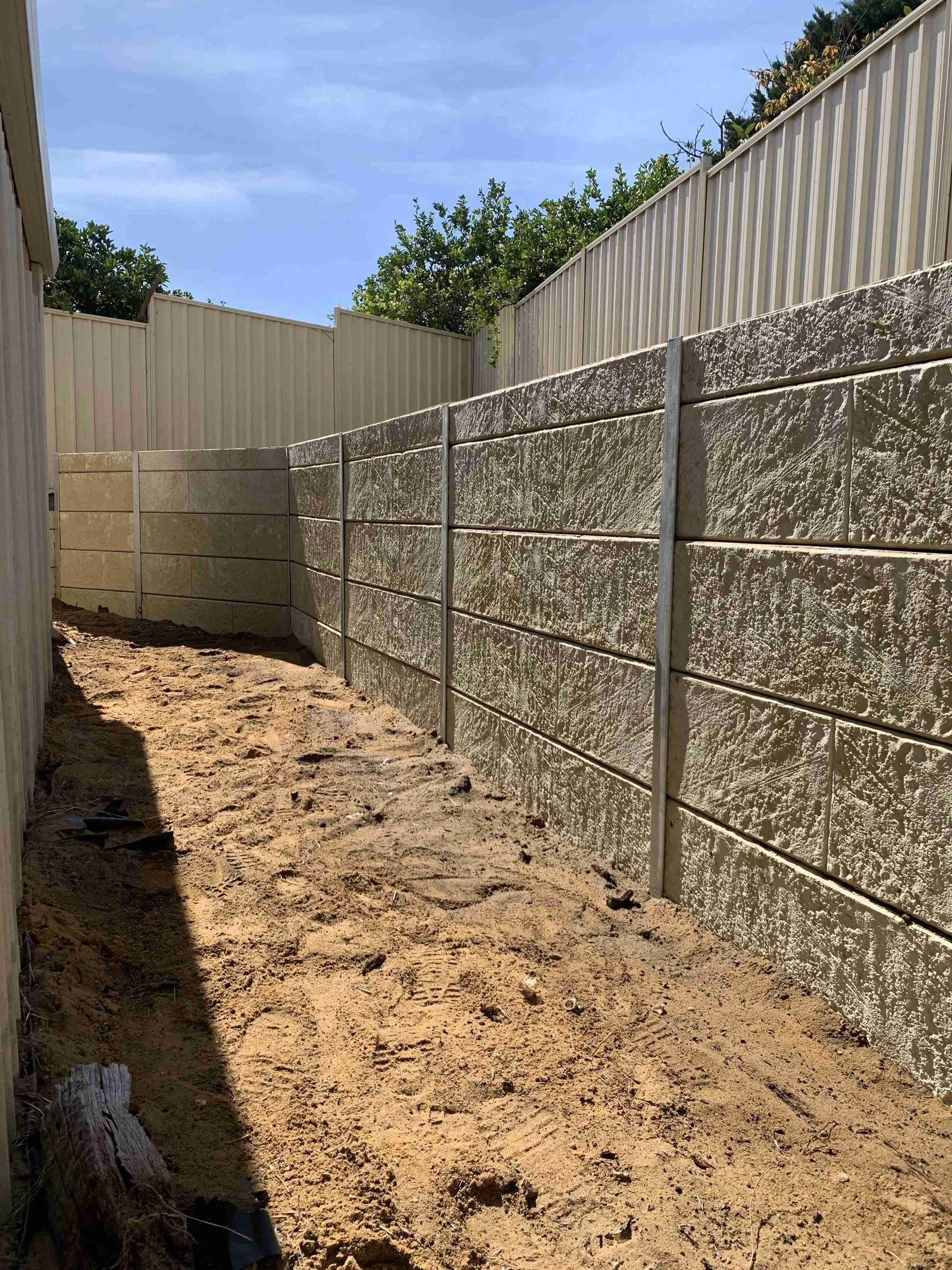 Textured panel retaining wall along a sandy side path, Perth